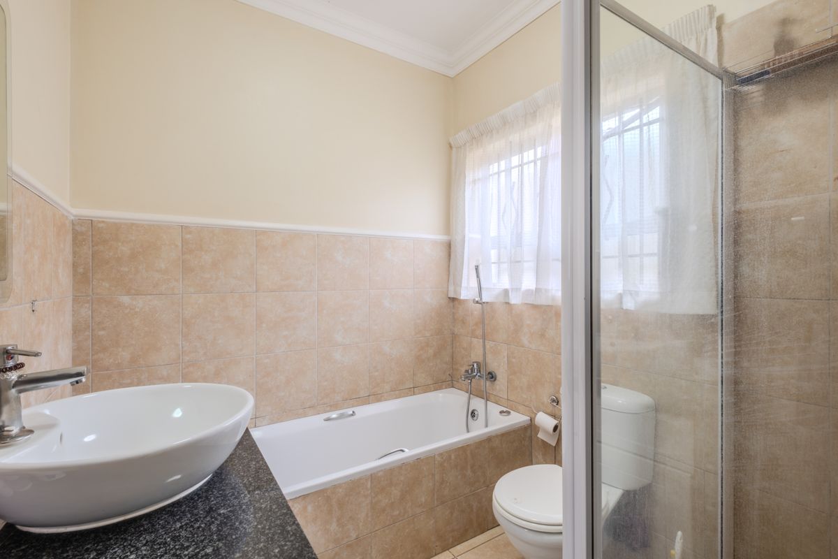 A functional bathroom featuring a vessel sink on a granite vanity, a built-in bathtub, and a separate shower enclosure with neutral wall tiling.