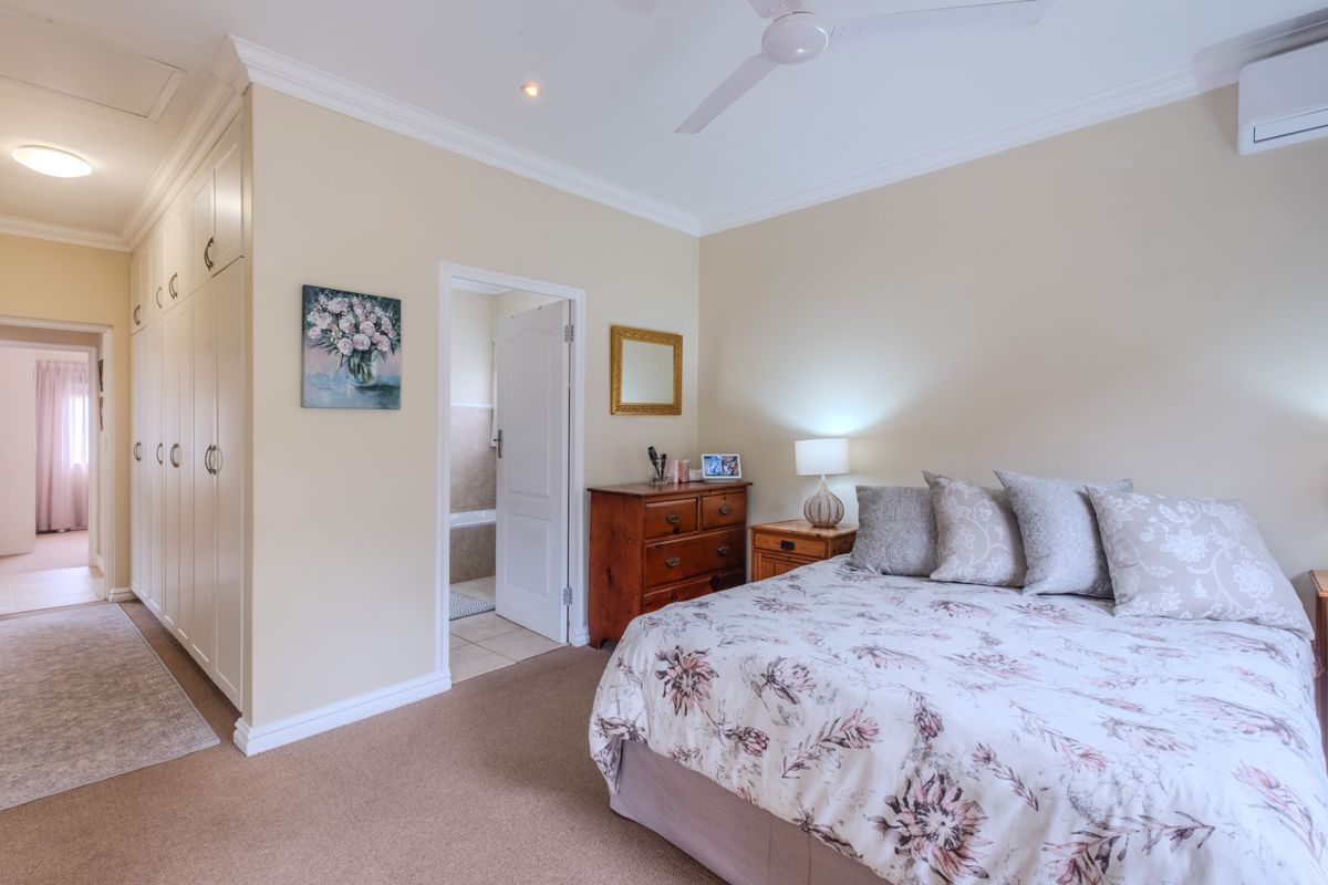 A well-maintained bedroom featuring built-in cupboards, a ceiling fan, and an integrated air conditioning unit, with an adjoining en-suite bathroom.