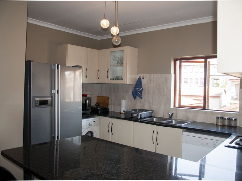 A functional kitchen featuring granite countertops, ample built-in cabinetry, a double stainless steel sink, and integrated hob with modern pendant lighting.