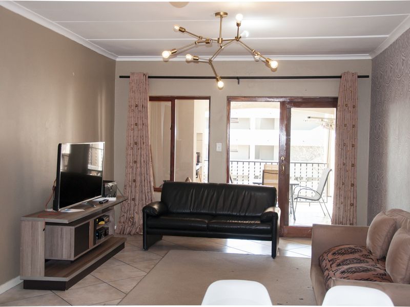 A living room featuring tiled flooring, a modern chandelier, and a sliding glass door providing access to an outdoor balcony area.