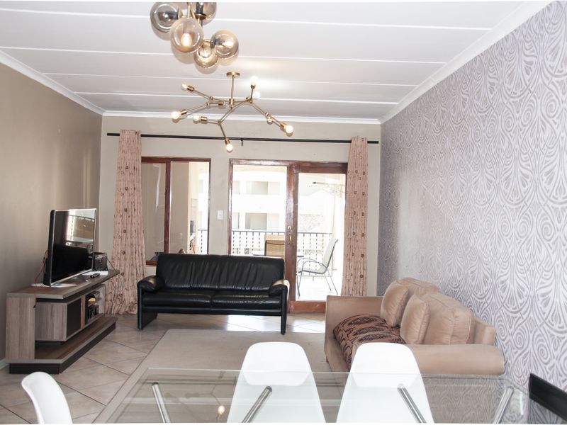 A living room featuring tiled flooring, patterned wallpaper, and a sliding glass door leading to an outdoor balcony area.