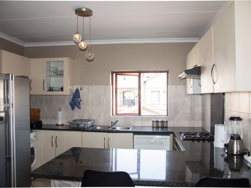 A functional kitchen featuring granite countertops, ample built-in cabinetry, a double sink, and an integrated electric hob with an extractor fan.