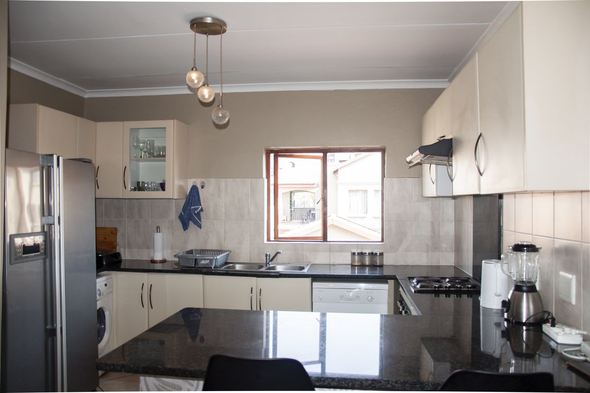 A functional kitchen featuring granite countertops, ample built-in cabinetry, a double sink, and an integrated electric hob with an extractor fan.