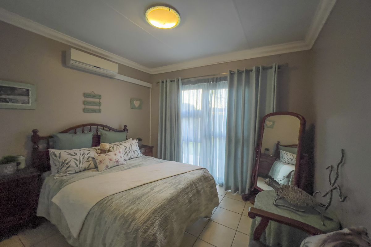 A comfortable bedroom featuring tiled flooring, a split-system air conditioner, and a sliding glass door providing natural light.
