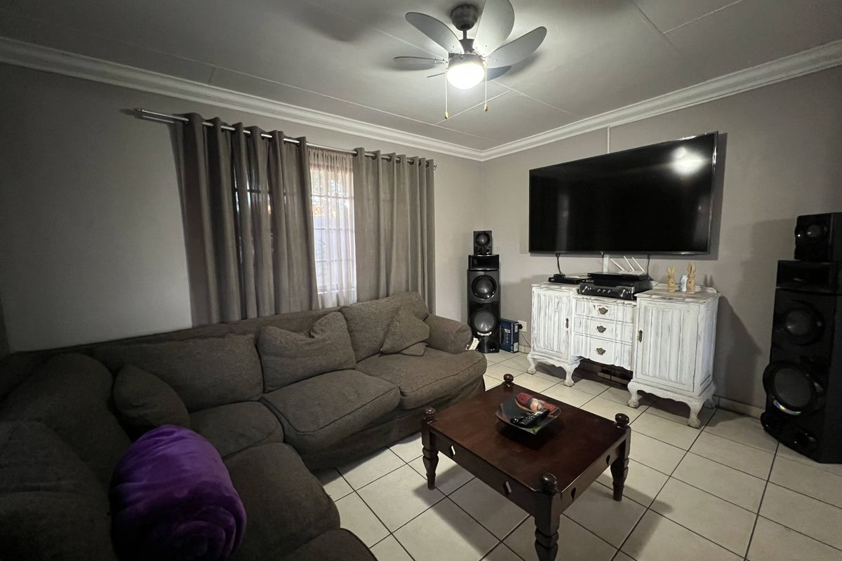 A comfortable living room featuring ceramic floor tiles, crown molding, and a ceiling fan, providing a functional space for relaxation.