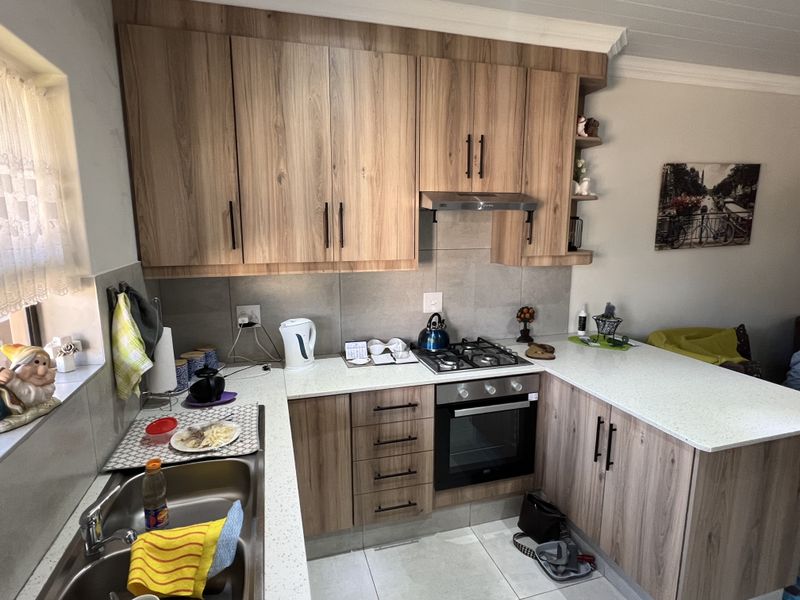 A functional kitchen featuring wood-look cabinetry, stone-style countertops, a built-in oven, gas hob, and stainless steel sink with tiled splashbacks.