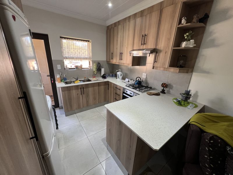 Modern kitchen featuring wood-look cabinetry, stone-style countertops, a built-in gas hob with extractor fan, and tiled flooring.