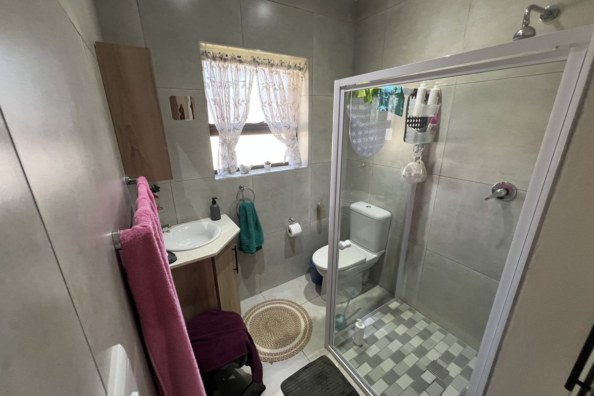 A compact, modern bathroom featuring floor-to-ceiling tiling, a glass-enclosed shower, a vanity basin, and a toilet.