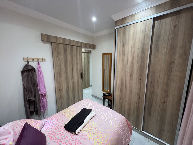 A well-maintained bedroom featuring built-in sliding door wardrobes, modern wood-look cabinetry, and recessed ceiling lighting.
