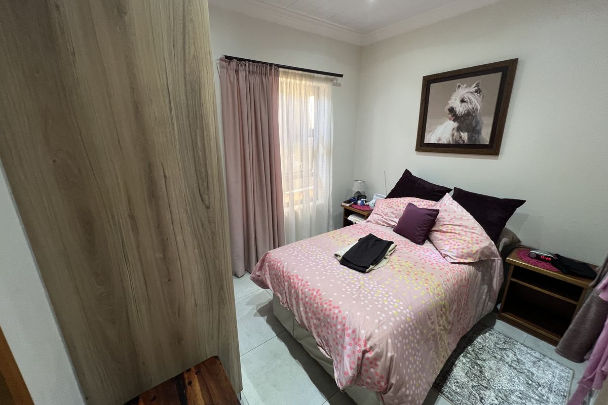 A well-maintained bedroom featuring neutral floor tiles, built-in wooden cabinetry, and a window with curtain treatments.