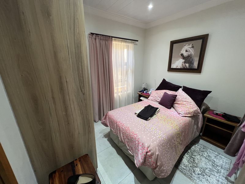 A well-maintained bedroom featuring neutral floor tiles, built-in wooden cabinetry, and a window with curtain treatments.