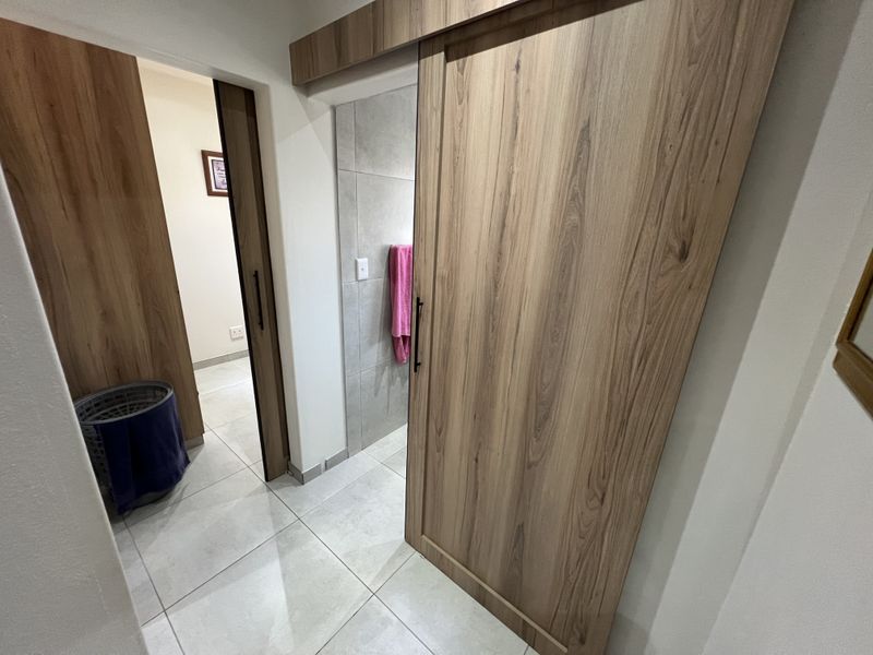 A hallway featuring modern wood-finish sliding doors and large format floor tiles, providing access to adjacent rooms.