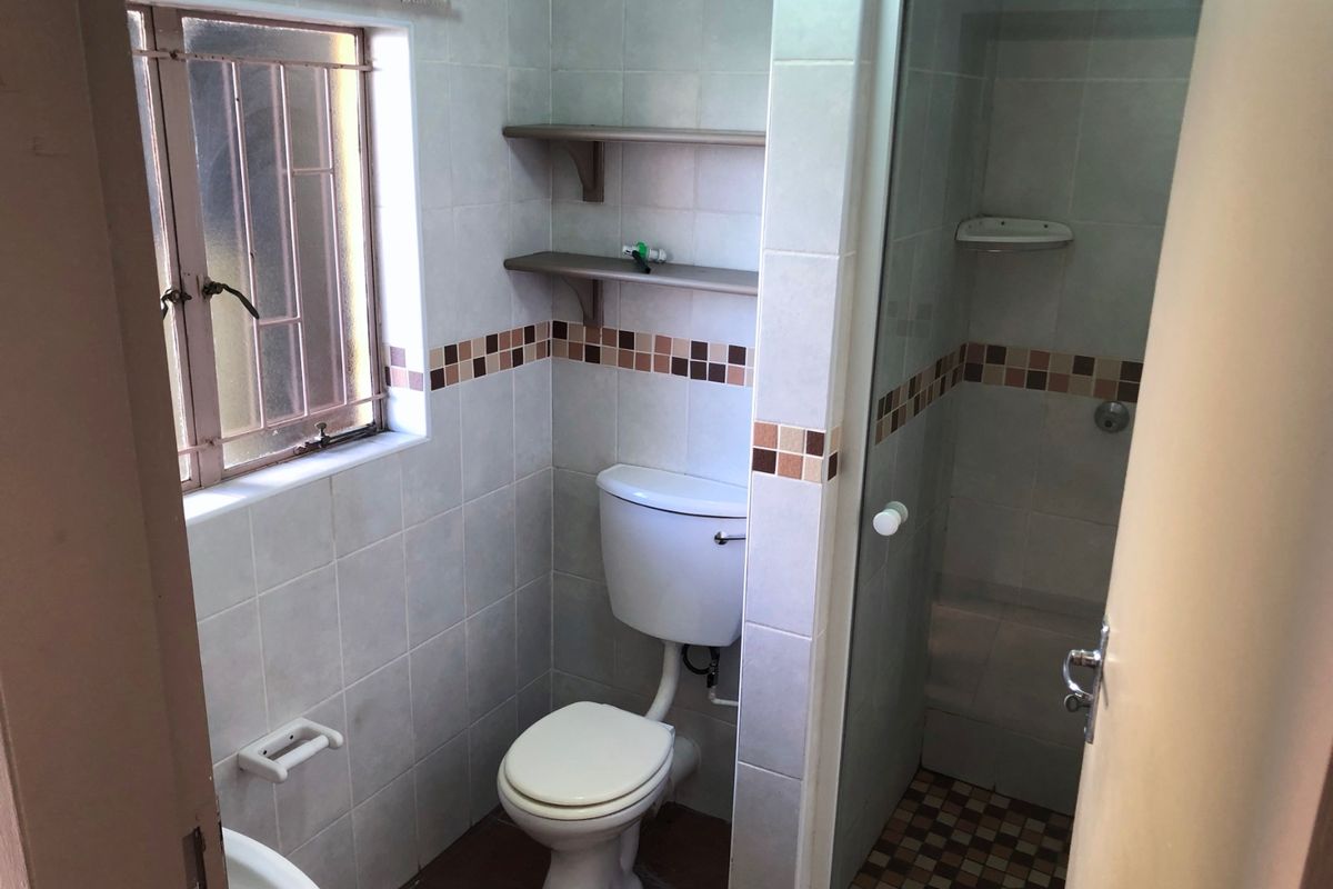 A compact bathroom featuring a shower enclosure, toilet, and tiled finishes. The space is functional but would benefit from modern updates.