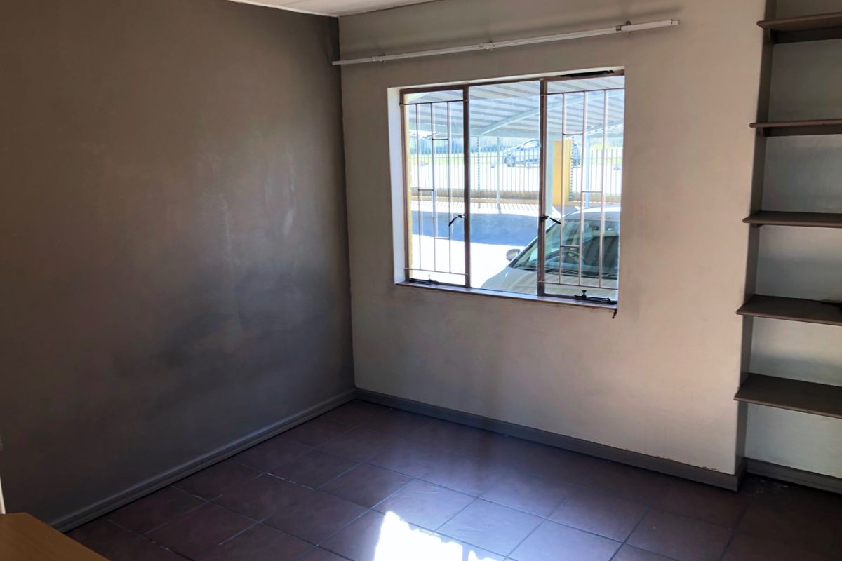 An empty bedroom featuring tiled flooring, built-in shelving, and a window with security bars, offering a blank canvas for potential updates.