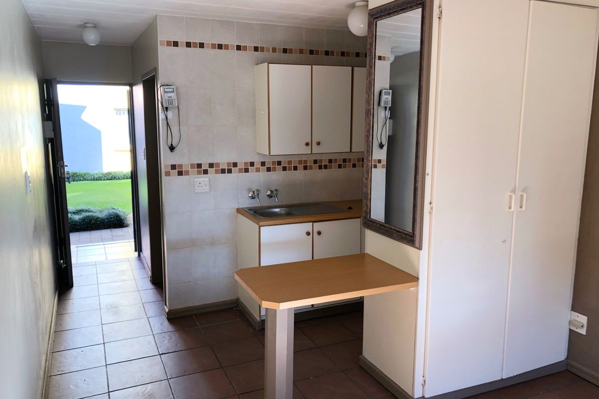 A compact kitchen area featuring built-in cabinetry, a stainless steel sink, tiled backsplash, and a breakfast bar, leading to an exterior entrance.