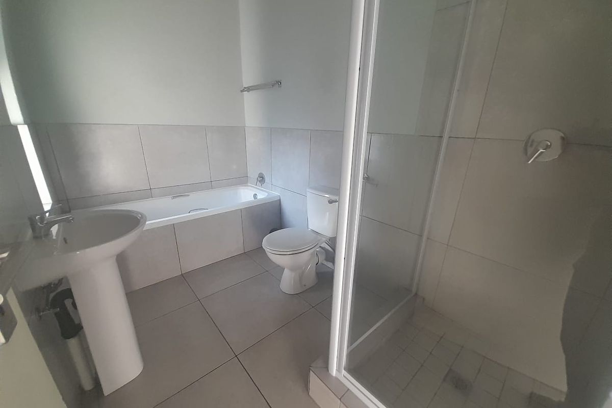 A functional bathroom featuring a pedestal sink, a built-in bathtub, a separate glass-enclosed shower, and a toilet with neutral floor and wall tiling.
