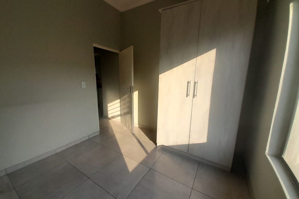 A bright bedroom featuring neutral floor tiles and a built-in wardrobe, offering a clean and functional living space.