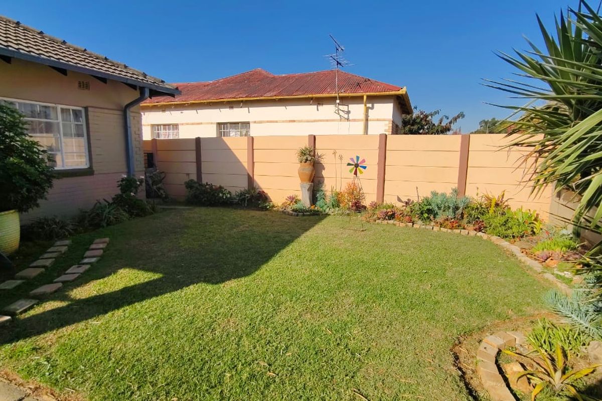 A private rear garden featuring a well-maintained lawn, landscaped garden beds, and a solid perimeter boundary wall.