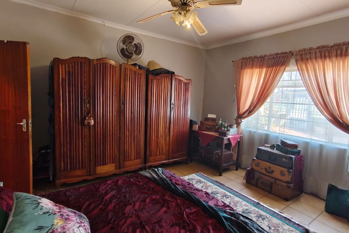 A bedroom featuring tiled flooring, a ceiling fan, and a window with security bars, providing a functional and traditional living space.