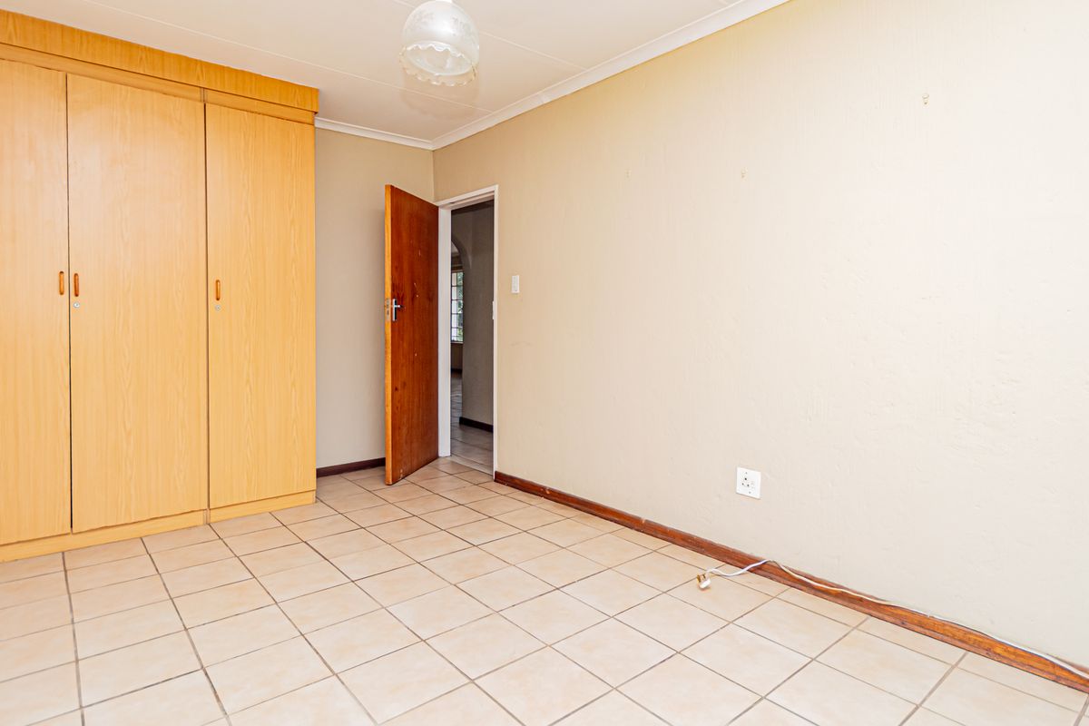 A vacant bedroom featuring neutral tiled flooring and a large built-in wooden wardrobe, offering a blank canvas for personalization.