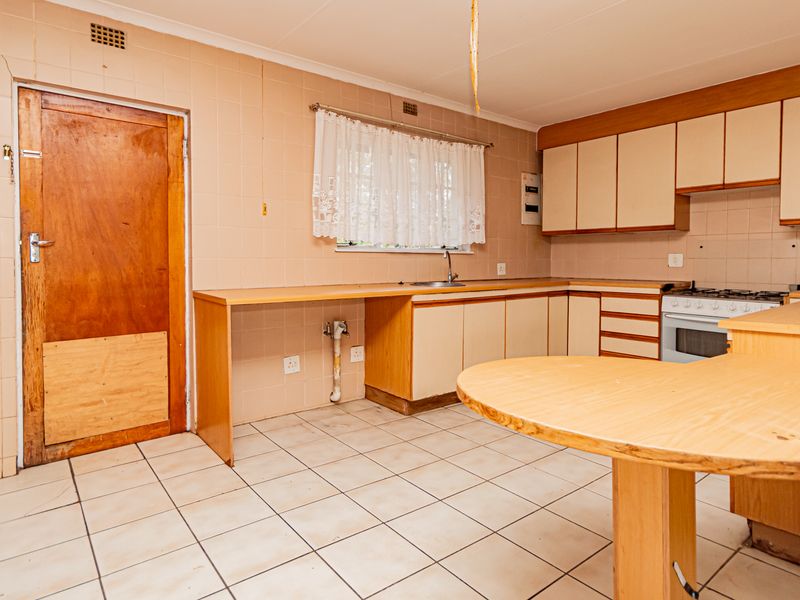 A dated kitchen featuring tiled walls and floors, built-in cabinetry, a breakfast bar, and a built-in oven with gas hob.
