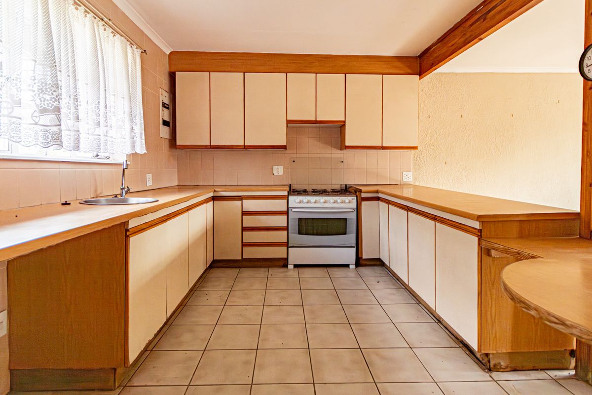 A functional kitchen featuring dated cabinetry, laminate countertops, a tiled backsplash, and a freestanding oven, offering potential for a modern renovation.