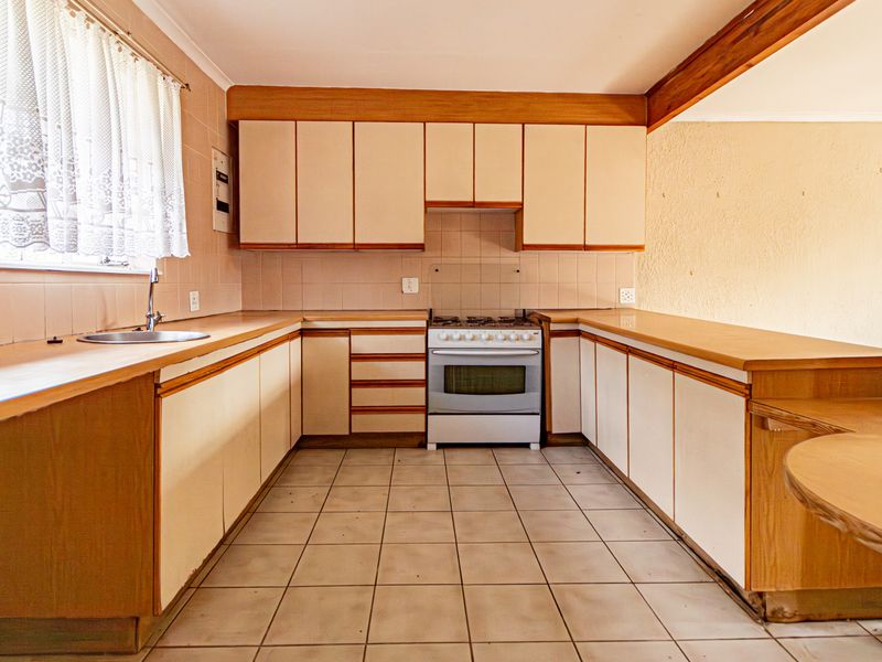A functional kitchen featuring dated cabinetry, laminate countertops, a tiled backsplash, and a freestanding oven, offering potential for a modern renovation.