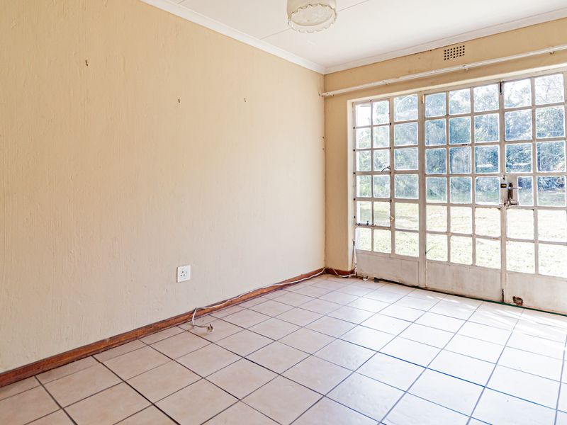 An empty living room featuring tiled flooring and large glass-paned french doors providing direct access to the garden.