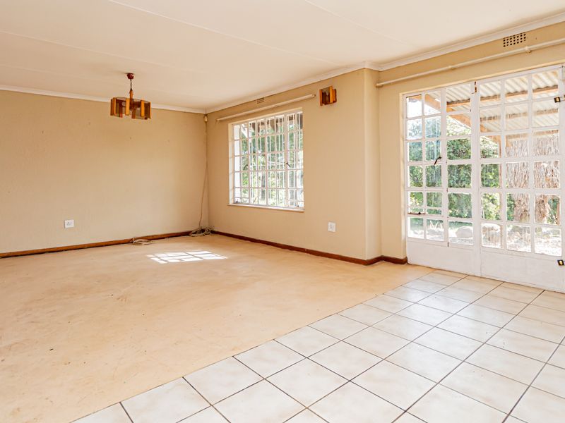 Spacious, empty living area featuring a mix of tiled and laminate flooring, large grid-pattern windows, and glass-paned french doors leading to the exterior.