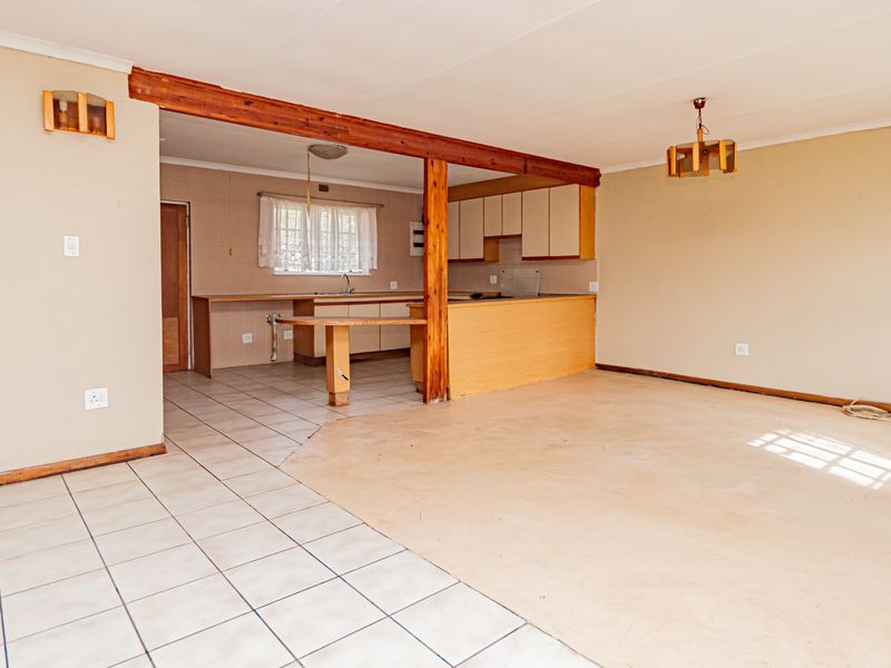 An open-plan living and kitchen area featuring tiled flooring, dated cabinetry, and an exposed timber beam, offering a blank canvas for renovation.