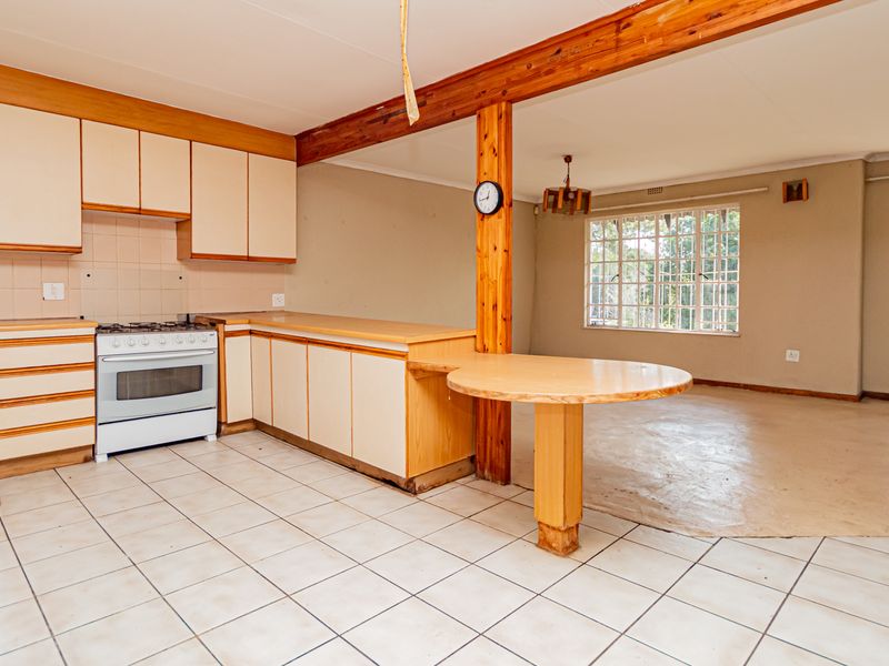 Spacious open-plan kitchen and living area featuring dated cabinetry, a gas stove, tiled flooring, and exposed timber structural elements.