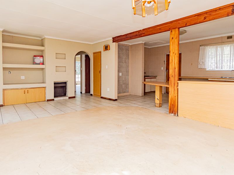 Spacious open-plan living and kitchen area featuring tiled floors, a built-in fireplace, timber structural beams, and integrated cabinetry, offering a blank canvas for renovation.