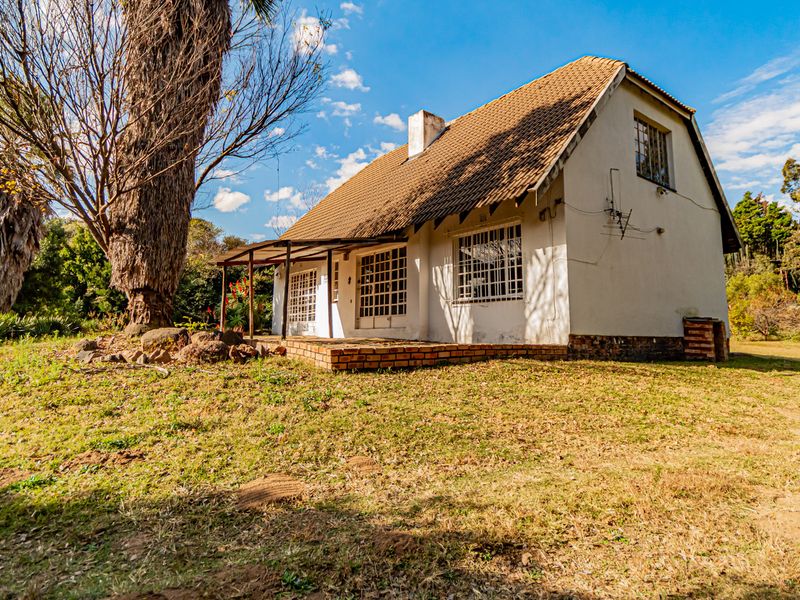 Rear view of a cottage featuring a tiled roof, covered veranda, and brick patio set within a large, established garden.