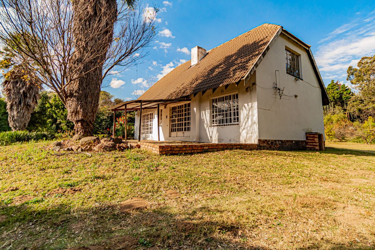 Rear view of a cottage featuring a tiled roof, covered veranda, and brick patio set within a large, established garden.