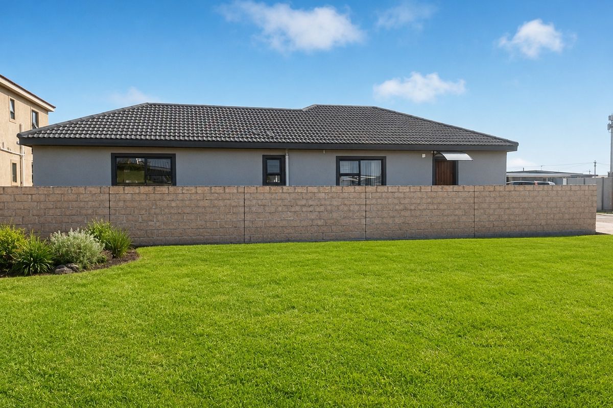 A view of the rear exterior of the house featuring a tiled roof, rendered walls, dark window frames, and a private lawn area.