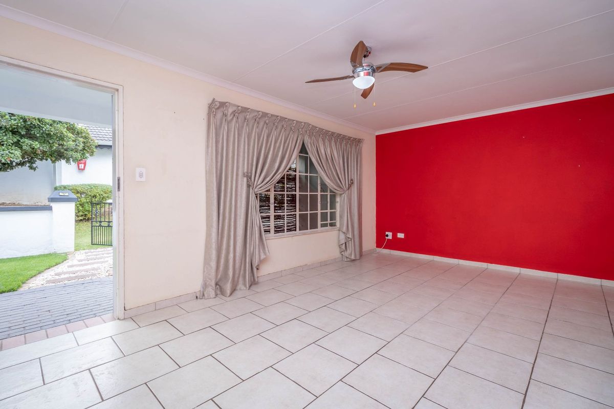 An empty living room featuring tiled flooring, a ceiling fan, and a bold red accent wall with direct access to the exterior.