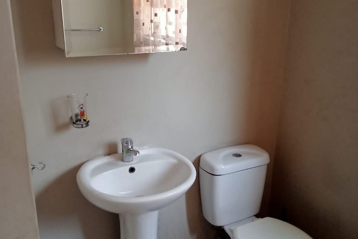 A functional guest bathroom featuring a white pedestal basin, a wall-mounted mirrored cabinet, and a standard toilet.