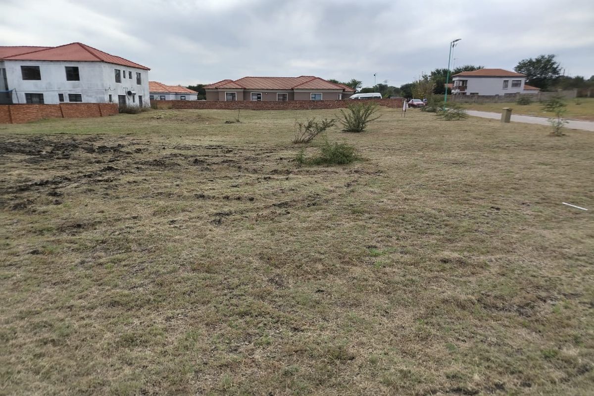 A vacant residential plot of land featuring grassed terrain and surrounding boundary walls in a developed neighborhood setting.