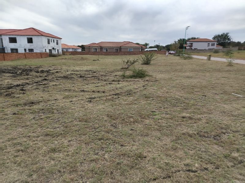 A vacant residential plot of land featuring grassed terrain and surrounding boundary walls in a developed neighborhood setting.