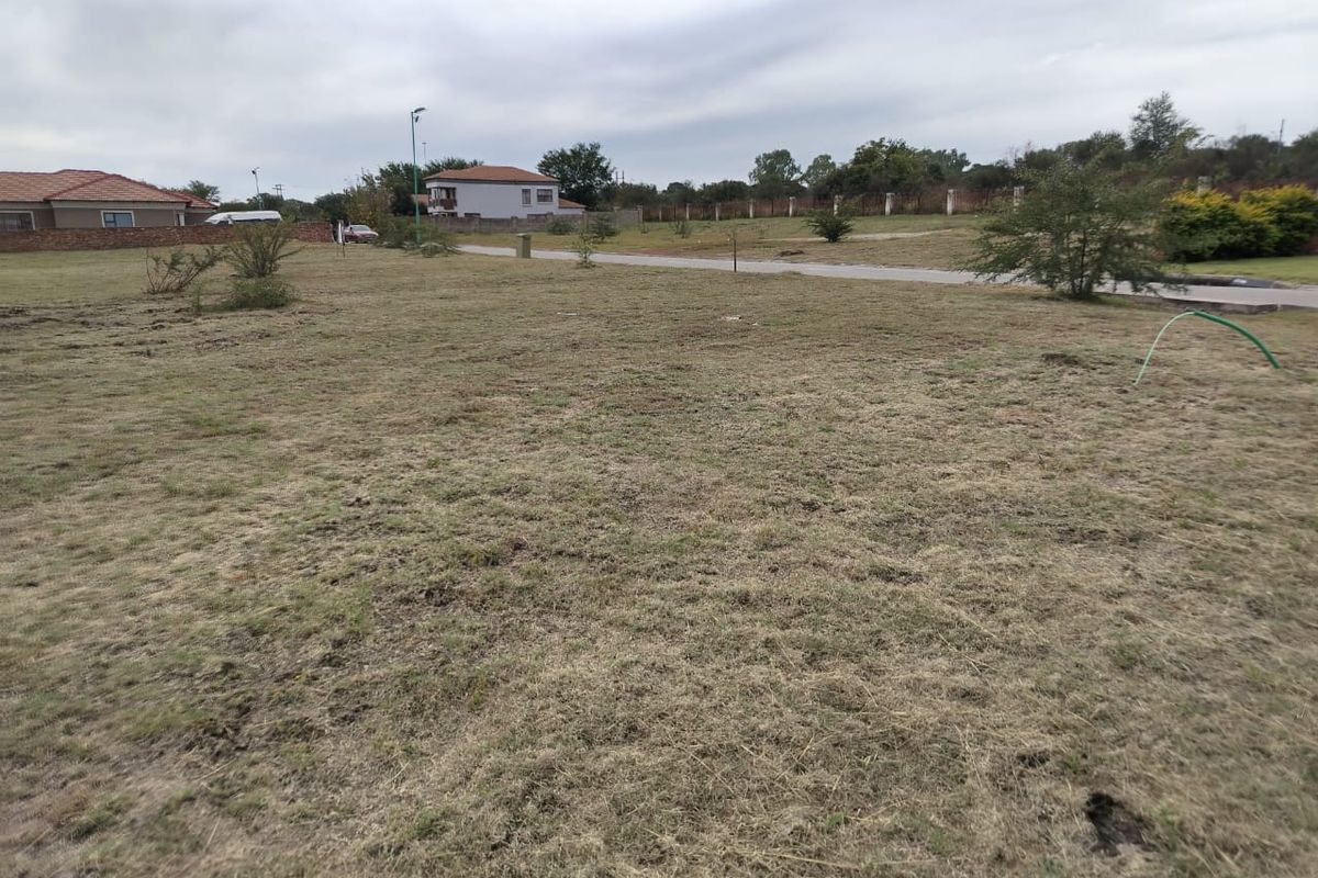 A vacant residential plot featuring a grass lawn with surrounding perimeter fencing and views of neighboring properties.