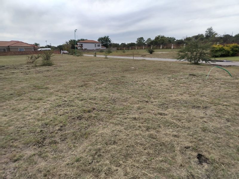 A vacant residential plot featuring a grass lawn with surrounding perimeter fencing and views of neighboring properties.