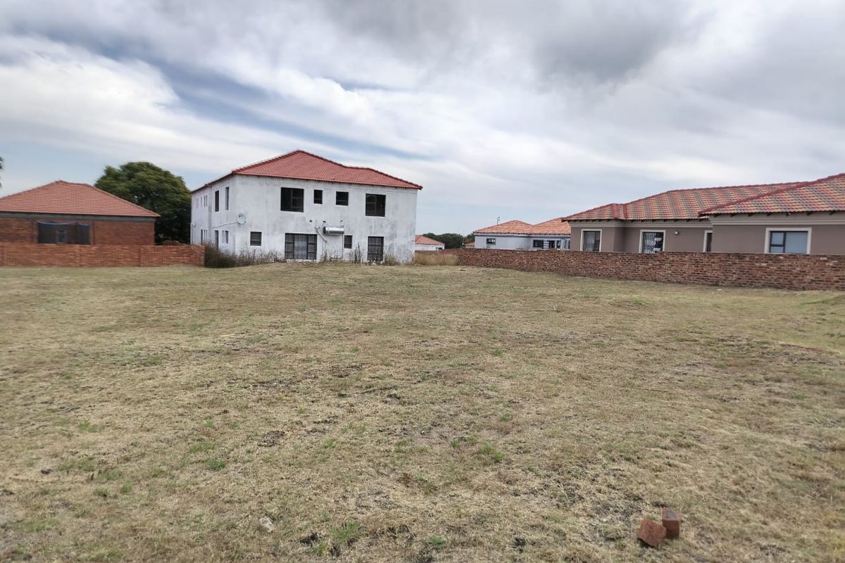 A view of a vacant residential plot featuring a brick boundary wall and surrounding residential properties with tiled roofs.