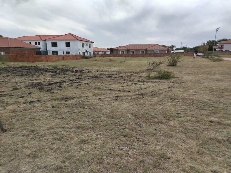 A vacant residential plot of land featuring natural grass cover and surrounding perimeter walls in a developed residential estate.