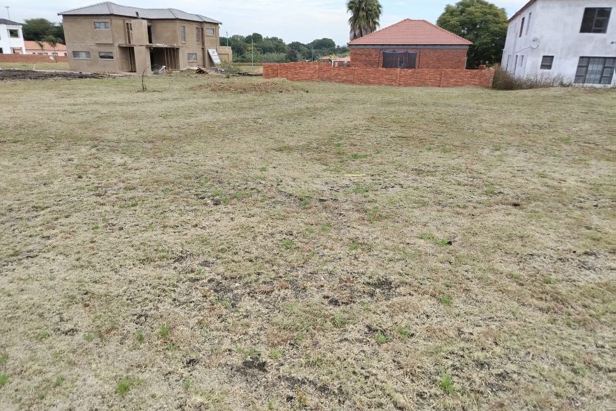 A vacant residential plot featuring open grassed land and a brick boundary wall, situated within a developing residential estate.