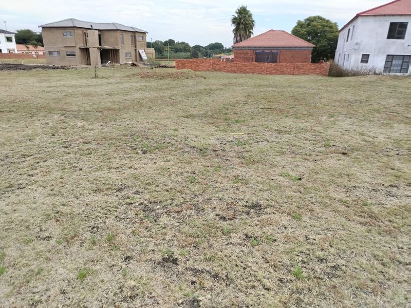 A vacant residential plot featuring open grassed land and a brick boundary wall, situated within a developing residential estate.
