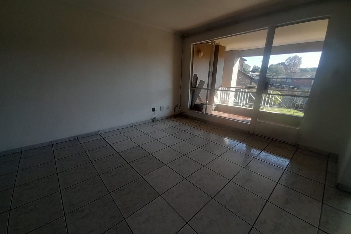 An empty living room featuring tiled flooring and a large sliding glass door providing access to an outdoor balcony area.