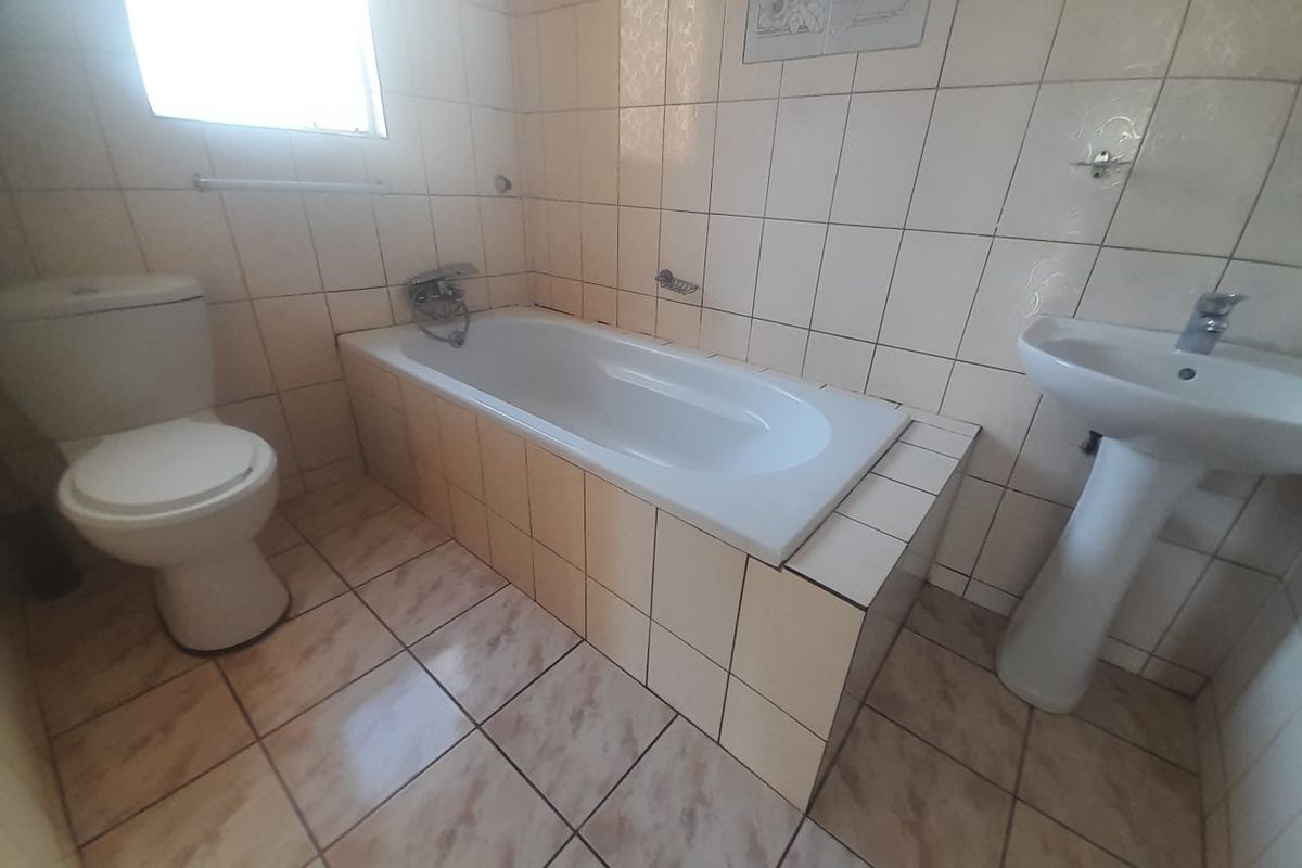 A dated bathroom featuring a standard bathtub, pedestal basin, and toilet with neutral wall and floor tiling.