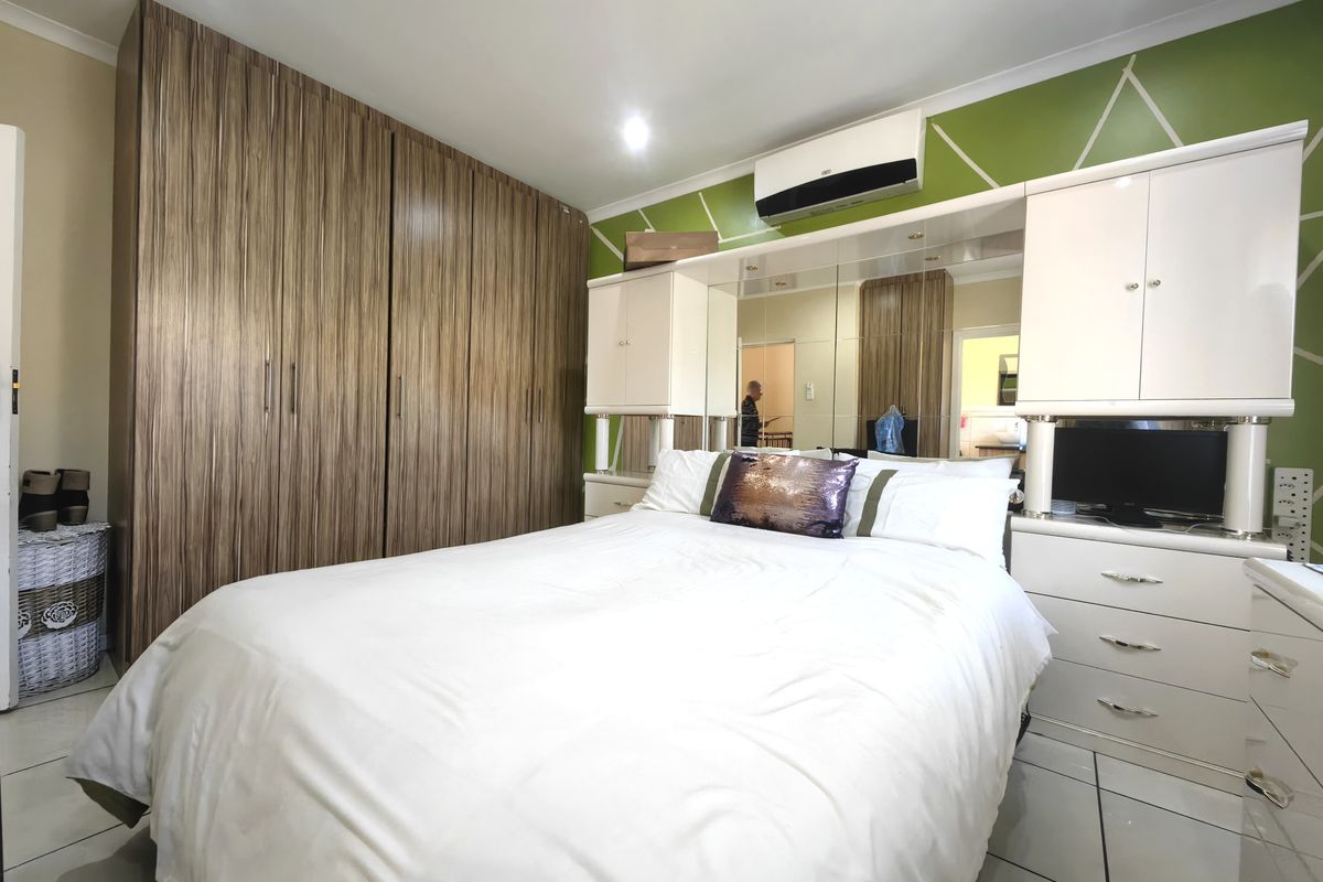 A bedroom featuring extensive built-in wooden cupboards, a mirrored headboard unit, tiled flooring, and a wall-mounted air conditioning unit.