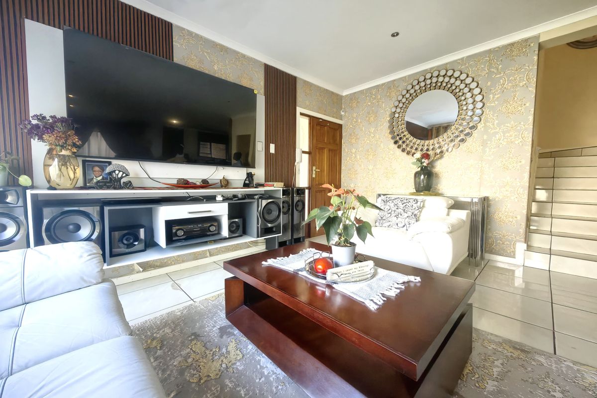 A well-maintained living room featuring tiled flooring, decorative wallpaper, and timber wall paneling, with an adjacent staircase leading to the upper level.