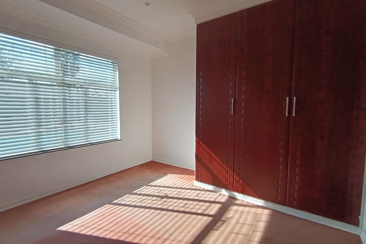 A bright, empty bedroom featuring built-in wooden cupboards, venetian blinds, and decorative cornice detailing.